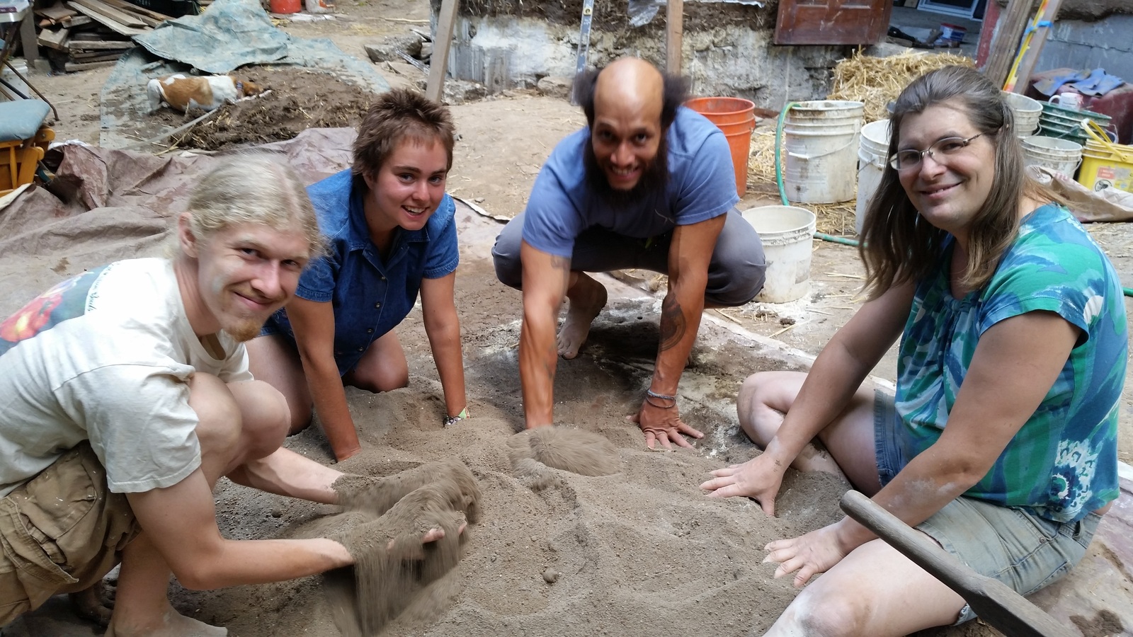 Four happy people turning sand and clay and straw into cob!